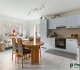 Dining room with wooden dining table, four chairs, couch with pillow, potted plant, kitchen with white cabinets, tile flooring, windows with mountain view