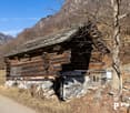 Wooden log house in mountains, stone foundation, metal gate, trees, road, mountain view