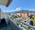 View of the balcony with furniture, greenery, distant mountain, and city.