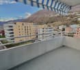 Balcony with tiled floor and railing, shaded by an awning, overlooking the cityscape and mountains