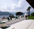 Spacious outdoor terrace with comfortable seating, a fireplace, and a scenic view of the lake and mountains in the background.