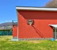 Two-story building with a red exterior, basketball hoop, and a grassy area in front. The building appears to be located in a mountainous area with a blue sky in the background.