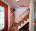 Entrance with wooden door, glass window, tiled floor, wooden stairs, wall with logs, storage under stairs, wooden handrail, wooden shelf, decorative items