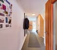 A hallway with a white wall, a wooden door, a rug, and a wooden cabinet with a clock on the wall.