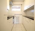 White kitchen with countertops, cabinets, oven, washing machine, tiled floor, window