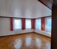 Hardwood flooring, white walls, white ceiling, 3 windows with red and white curtains, central heating under window sills