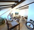 modern attic room, wooden beams, wooden dining table, white walls, wooden floor, bicycles, bookshelves, laptop, armchair, window, radiator