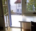 open door to balcony, glass railings, large window with view, wooden floor, desk, chair