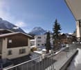 View of a building's balcony, cars parked in front, snowy mountains in the background