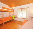 Wooden bunk bed, orange bedding, green chair, wooden ceiling, curtains, hardwood floor