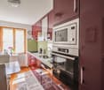 Modern kitchen with red cabinets, stainless steel appliances including a microwave and oven, hardwood floors, and a window providing natural light.