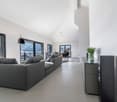 large windows, grey L-shaped sofa, dark floor, black speaker, floor to ceiling windows, balcony
