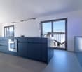 Modern kitchen with blue cabinets, stainless steel oven, island, large glass doors leading to a balcony, and a view of the mountains.