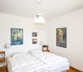 Bedroom with two single beds, hanging lamps, pictures on the wall, wooden nightstand, wooden wall outlet and plug