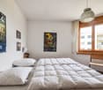 white walls, white bedspread, bed, 2 pillows, lamp, 3 paintings, chair, window, piano