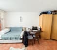 small room with a bed, desk, two chairs, cabinet with books, microwave, and storage boxes