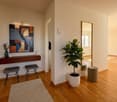 Entrance hallway with wooden floor, large mirror, stool, decorative plant, console table with flower vase, wall mounted light