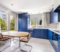 modern kitchen, wooden table, blue cabinets, white countertop, large window, view of outside