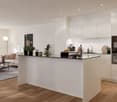 The image shows an open concept living room and kitchen area with a modern, minimalist design. The kitchen features white cabinets, a black countertop, and a built-in dishwasher. The living room has a beige sofa and a coffee table. The space is bright and
