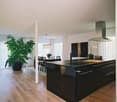 Open plan kitchen and dining room with wooden floor, chandelier lighting, modern black island with marble countertop, kitchen sink, gas range, and dining table with chairs