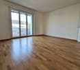 Empty room with wooden flooring, sliding glass doors leading to a balcony, white walls and ceiling, power outlets