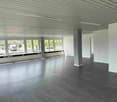 Large open space with high ceilings, gray walls, and a hardwood floor. The space has large windows overlooking the street outside.