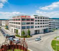 Office building, white exterior, multiple windows, multiple floors, red roof signage for Migros and Denner