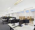 Open office space with rows of desks, computers, and monitors. Large windows provide natural light. Decorative bamboo sticks are placed around the room.