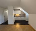 Attic apartment with slanted ceilings, open-plan kitchen and living area, hardwood floors, white cabinets, and a dishwasher in the kitchen
