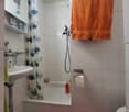 Tiled bathroom with a bathtub, shower curtain with a fish pattern, an orange towel, and a shelf with toiletries.