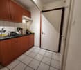 Compact kitchen with wooden cabinets, tiled floor, gas stove, and various kitchen appliances and utensils