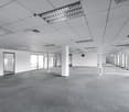 Empty office room with white walls, tiled floor, large windows, pillars, ceiling lights