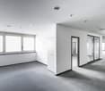 an empty room with white walls and gray flooring, large glass windows, and several doors
