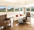 Wooden floor, modern couch, two armchairs, center table, large windows with balcony, vase with flowers