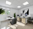 Modern office space with white walls, suspended ceiling tiles, large windows, desk with computer setup, office chairs, and a potted plant.