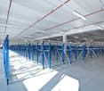 Large industrial warehouse space with rows of blue metal shelving units and overhead lighting