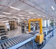 Large industrial warehouse with shelving units, conveyor belts, and a forklift operating in the center of the space.