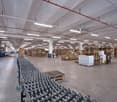 Large industrial warehouse space with high ceilings, rows of shelving and pallets stacked with goods, and a fleet of shopping carts or trolleys in the foreground.