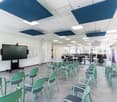 Large open office space with white walls, gray flooring, and green chairs. The ceiling has blue acoustic panels and there is a large projector screen mounted on the wall.