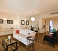 a bright living room with wooden flooring, white sofa, glass coffee table, and black armchairs