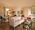 white living room with white and gray couch, white table and chairs, large white cabinet, mirror, lamps