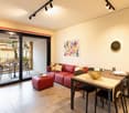 modern living room, red sofa, wooden dining table, white table runners, modern paintings, black modern chairs, sliding doors to the balcony, balcony with plants
