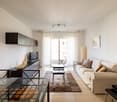 Modern living room with white walls, beige sofa, wooden floor, glass table, TV, and a balcony with sliding glass doors