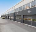 Industrial building with multiple garage doors, yellow van parked in front, gray exterior, glass windows, number 16 on the right side