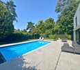 Outdoor swimming pool with deck, lounge chairs, tables, hedges, trees, and grassy areas