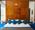 master bedroom with large bed, blue pillows, wooden wall, 2 nightstands, and mirrors