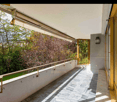 ample balcony with metal railings, shaded by an awning, tiled floor, view of greenery, golden railings