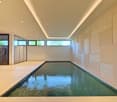 rectangular indoor pool with glass walls and reflective ceiling, wooden floor, white walls, illuminated by recessed lighting