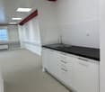 empty room, with white tiled floor, white walls, a kitchen counter, sink, cabinets and a ceiling lamp