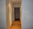 Empty hallway, hardwood floor, white walls, light switch.